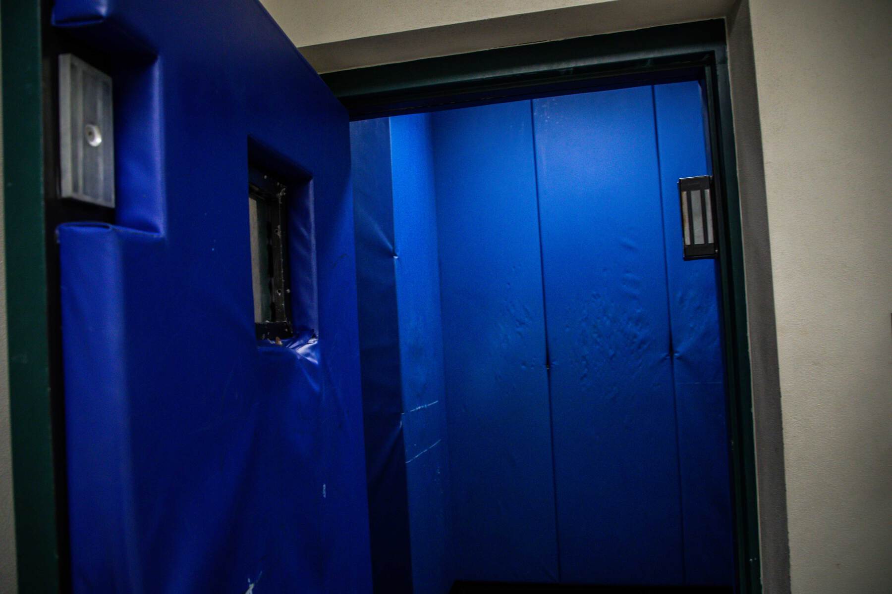Blue padded seclusion room with a small observation window and padded walls