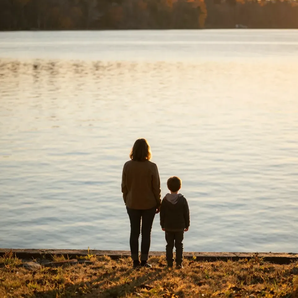 A parent and child look over a calm Ontario lake at sunset, seen from behind
